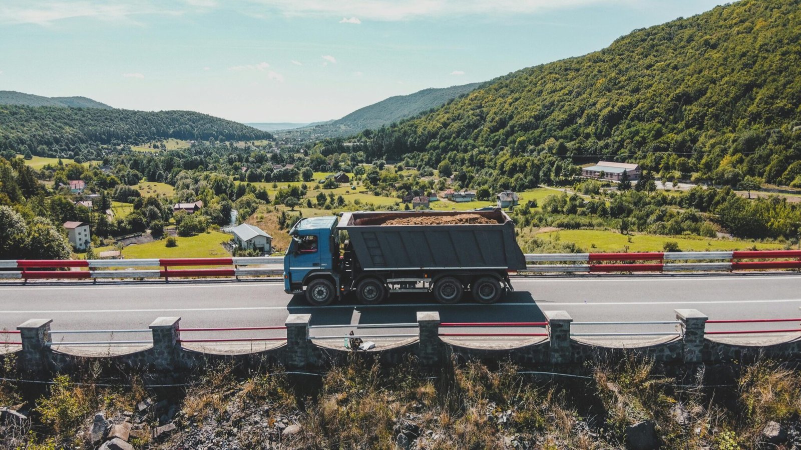 Blue truck driving on a mountain highway in Romania, with a scenic landscape view.