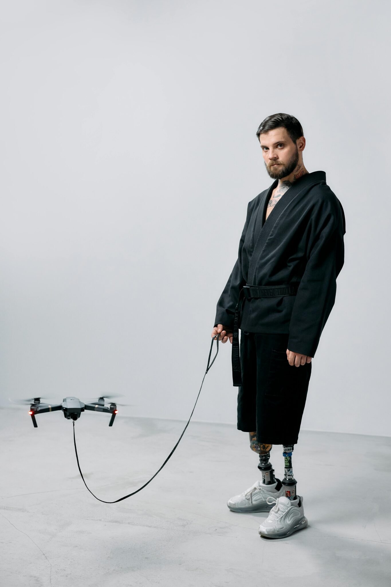 Adult male with prosthetic legs stands in a studio beside a drone, showcasing modern technology.