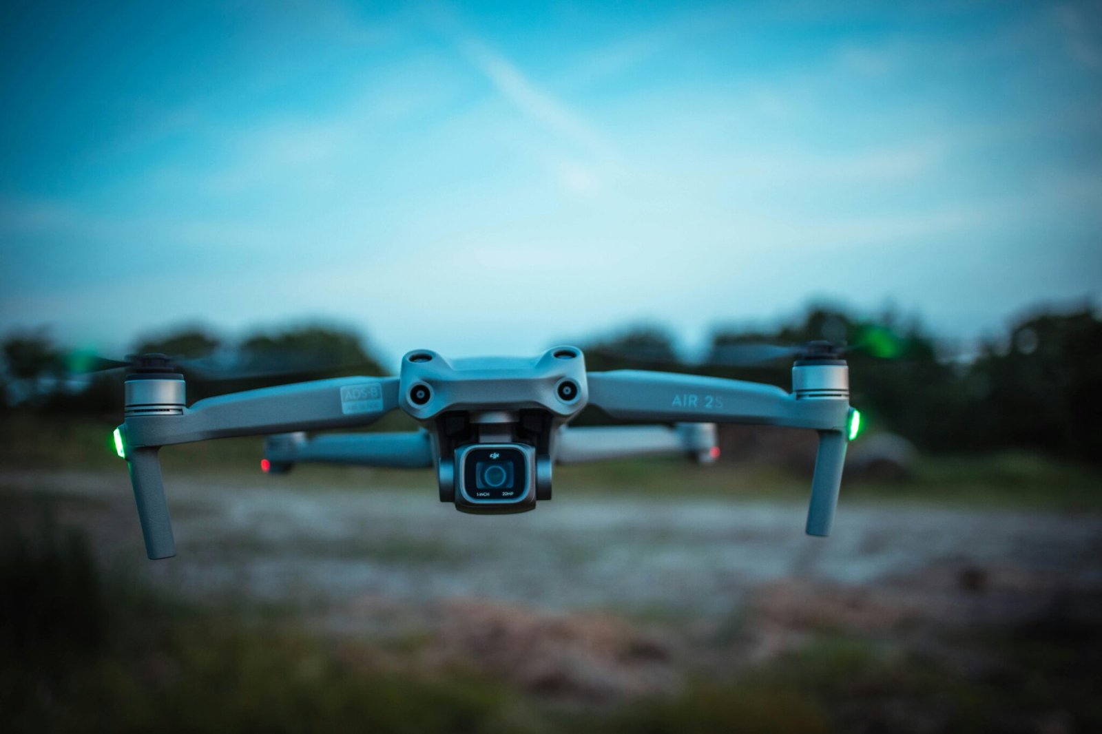 Close-up of a modern quadcopter drone with lights, hovering over a blurred outdoor background.