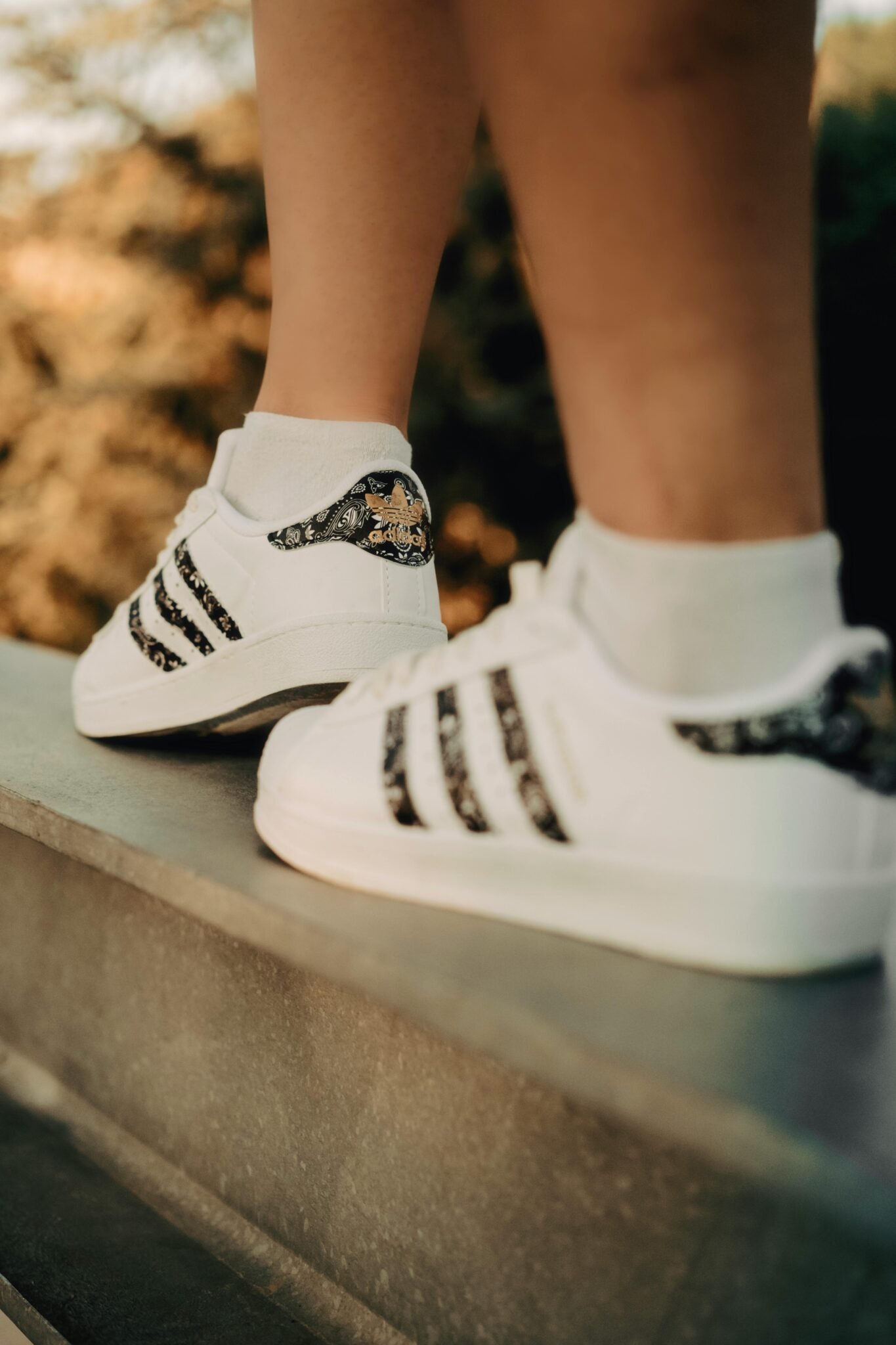 Close-up of white sneakers with black accents on a metal ledge, outdoors.