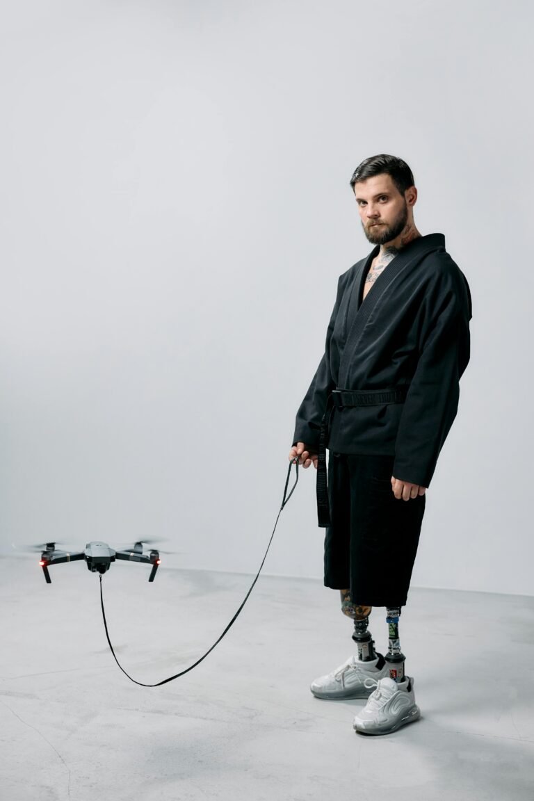 Adult male with prosthetic legs stands in a studio beside a drone, showcasing modern technology.