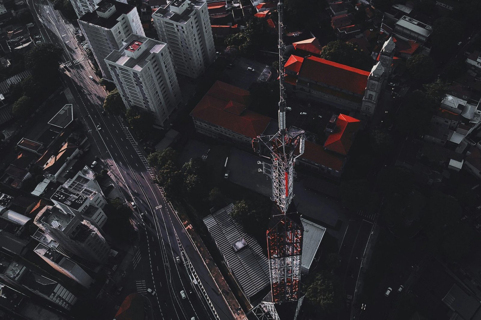 Drone captures vibrant cityscape with towering communication mast at dusk.