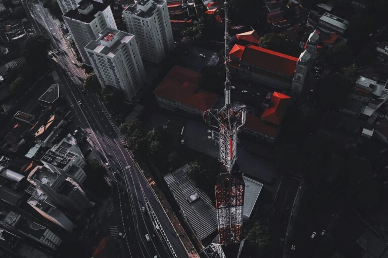 Drone captures vibrant cityscape with towering communication mast at dusk.