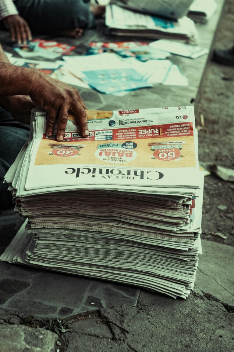 Close-up of a hand sorting newspapers on a pavement, outdoors.